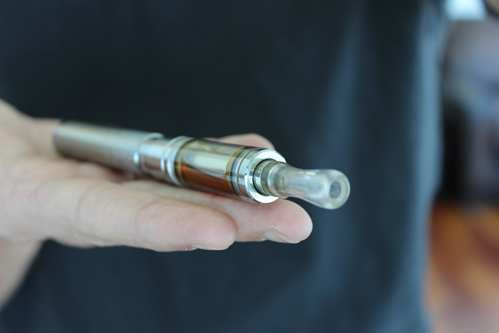 Hand holding a silver vape pen against a dark background